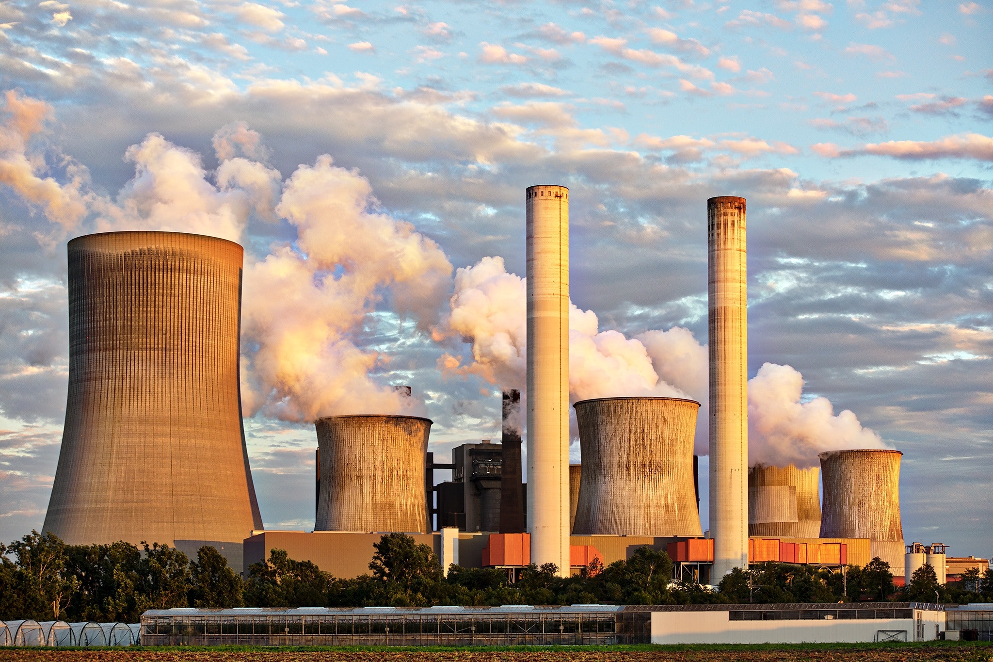 A picture of a factory in the distance letting out metric tons of pollution into the atmosphere to show the need for compliance standards that hold organizations responsible for their actions.