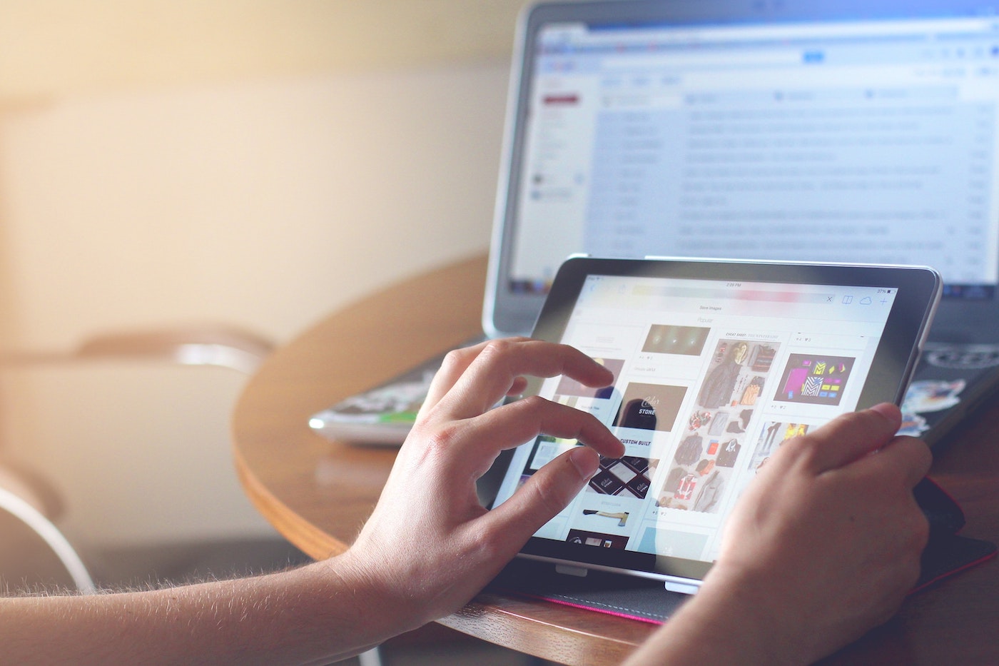 Image of person scrolling on tablet with computer screen in the background displaying email inbox. Meant to symbolize direct marketing.